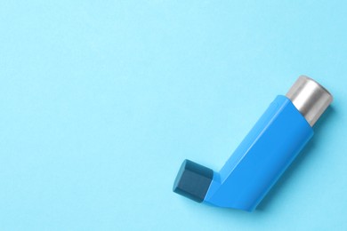 Photo of Asthma inhaler on light blue background, top view. Space for text