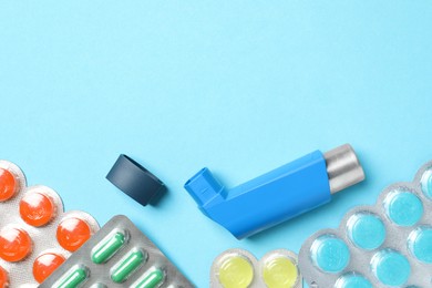 Photo of Asthma inhaler and pills on light blue background, flat lay. Space for text