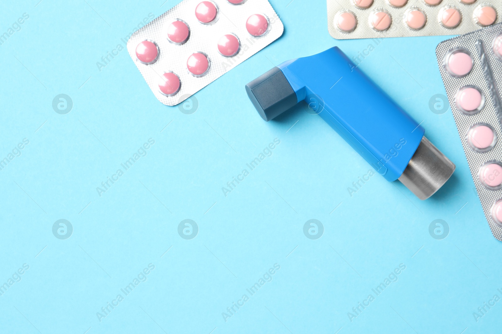 Photo of Asthma inhaler and pills on light blue background, flat lay. Space for text