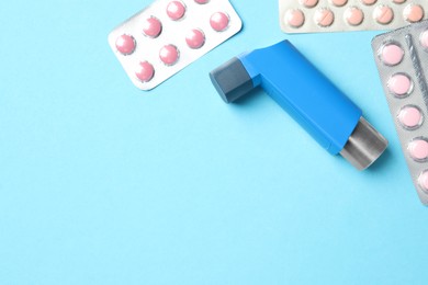 Photo of Asthma inhaler and pills on light blue background, flat lay. Space for text