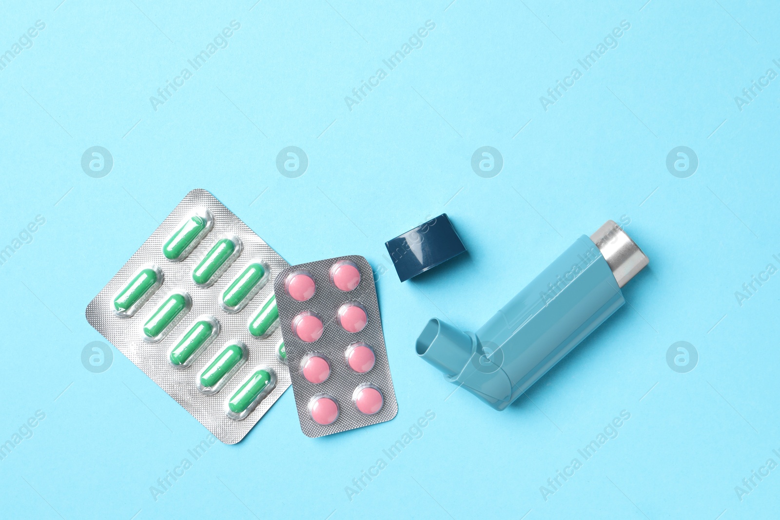 Photo of Asthma inhaler and pills on light blue background, flat lay