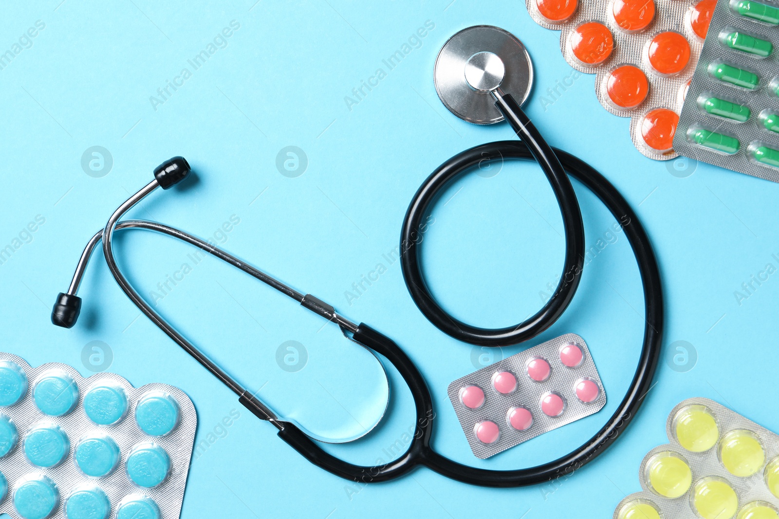 Photo of Stethoscope and pills on light blue background, flat lay