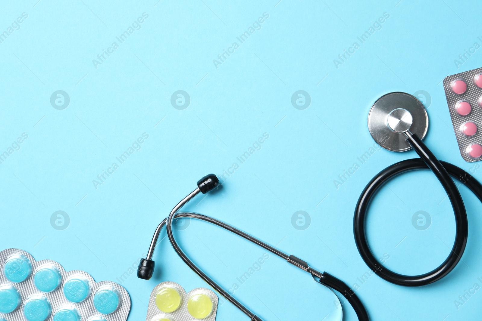 Photo of Stethoscope and pills on light blue background, flat lay. Space for text