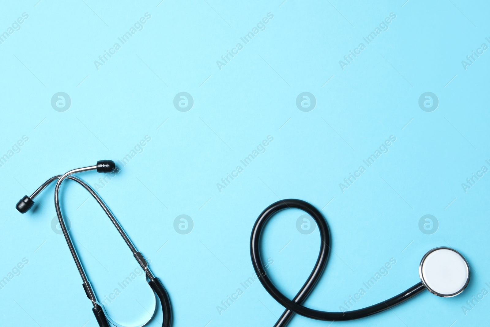 Photo of Stethoscope on light blue background, top view. Space for text