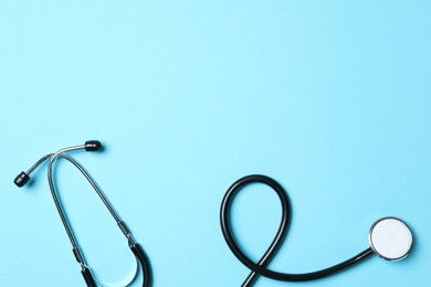 Photo of Stethoscope on light blue background, top view. Space for text