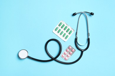 Photo of Stethoscope and pills on light blue background, flat lay