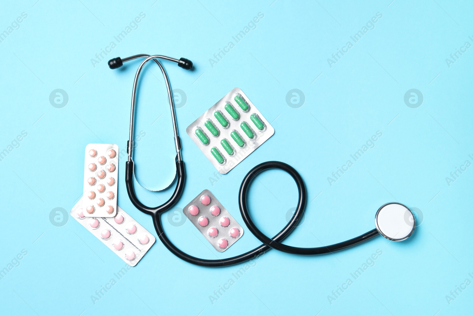 Photo of Stethoscope and pills on light blue background, flat lay