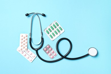 Photo of Stethoscope and pills on light blue background, flat lay