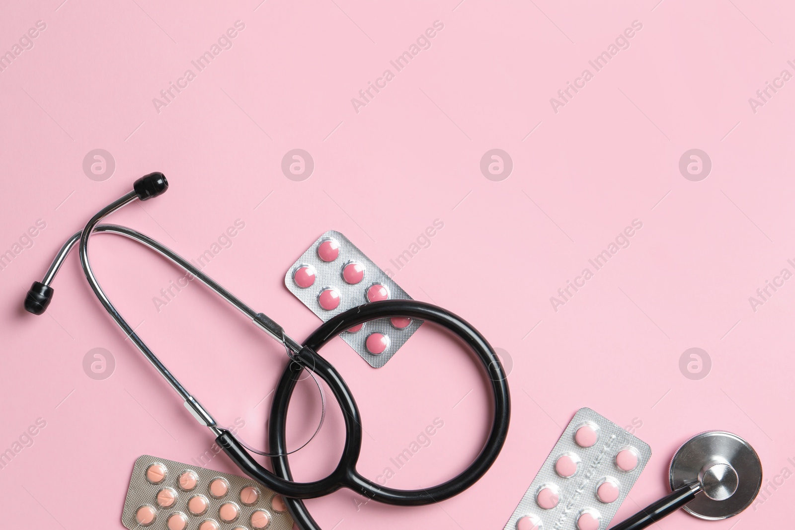 Photo of Stethoscope and pills on pink background, flat lay. Space for text