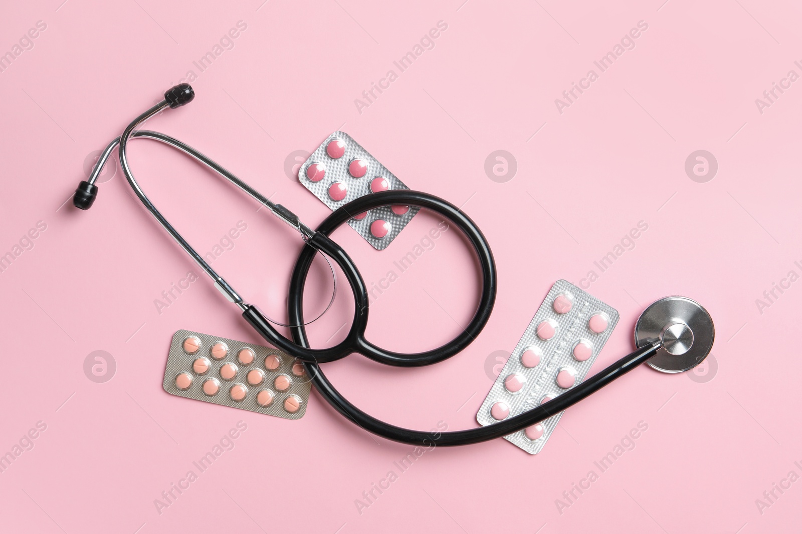 Photo of Stethoscope and pills on pink background, flat lay