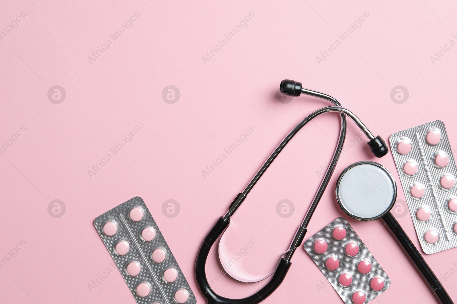 Photo of Stethoscope and pills on pink background, flat lay. Space for text