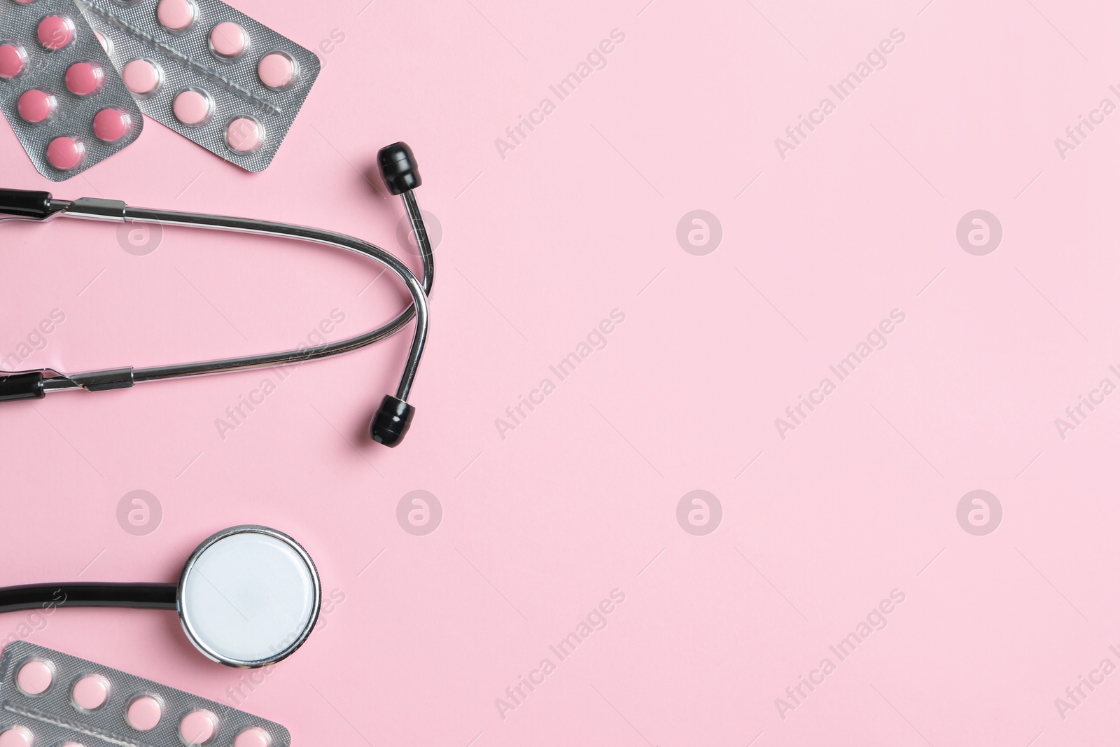 Photo of Stethoscope and pills on pink background, flat lay. Space for text