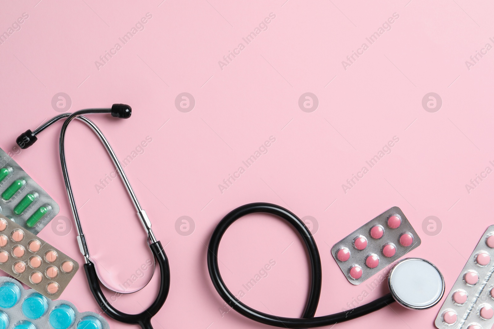 Photo of Stethoscope and pills on pink background, flat lay. Space for text