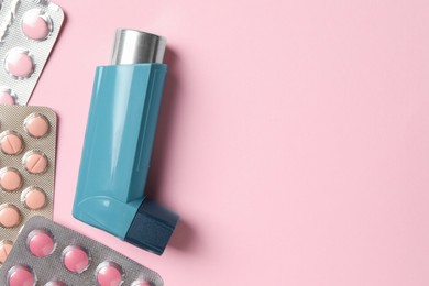 Photo of Asthma inhaler and pills on pink background, flat lay. Space for text