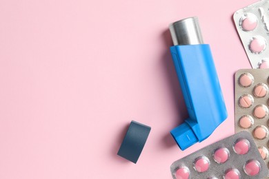 Photo of Asthma inhaler and pills on pink background, flat lay. Space for text