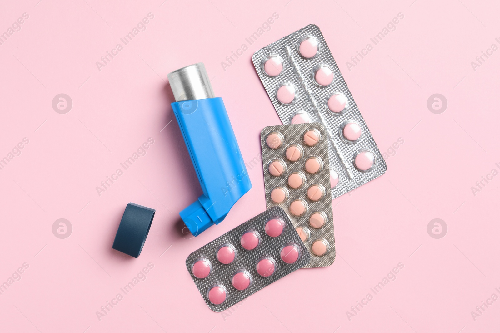 Photo of Asthma inhaler and pills on pink background, flat lay