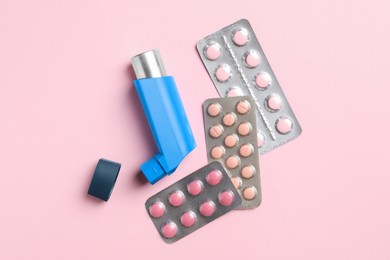 Photo of Asthma inhaler and pills on pink background, flat lay