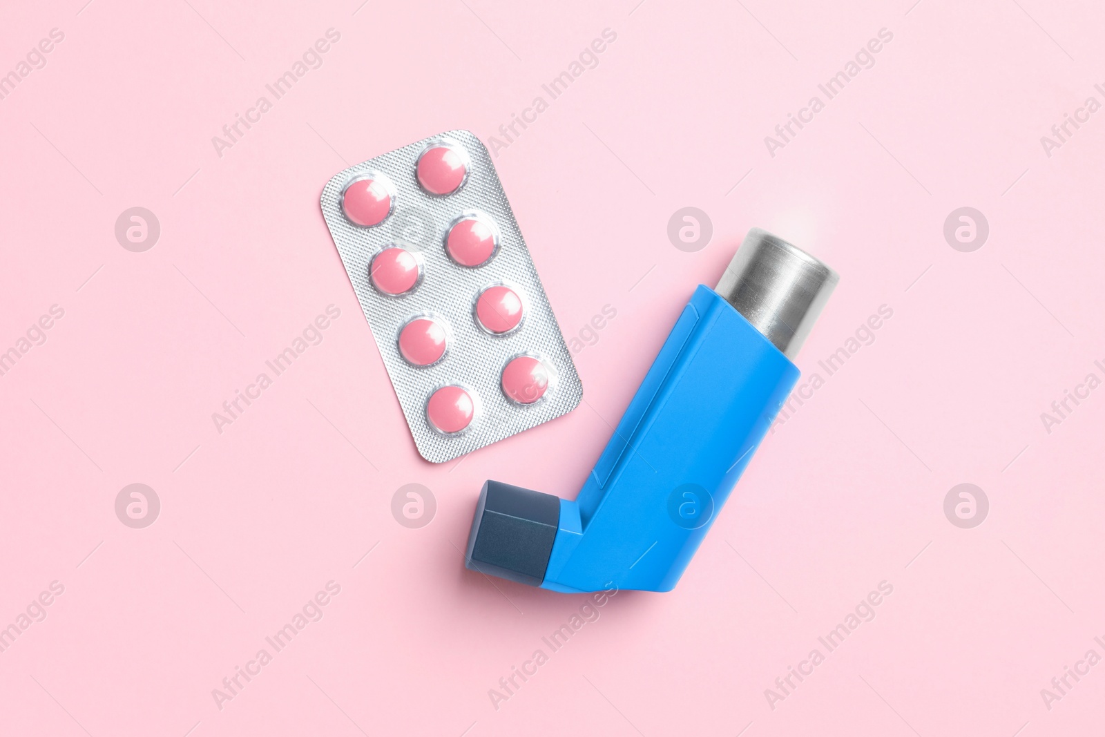 Photo of Asthma inhaler and pills on pink background, flat lay