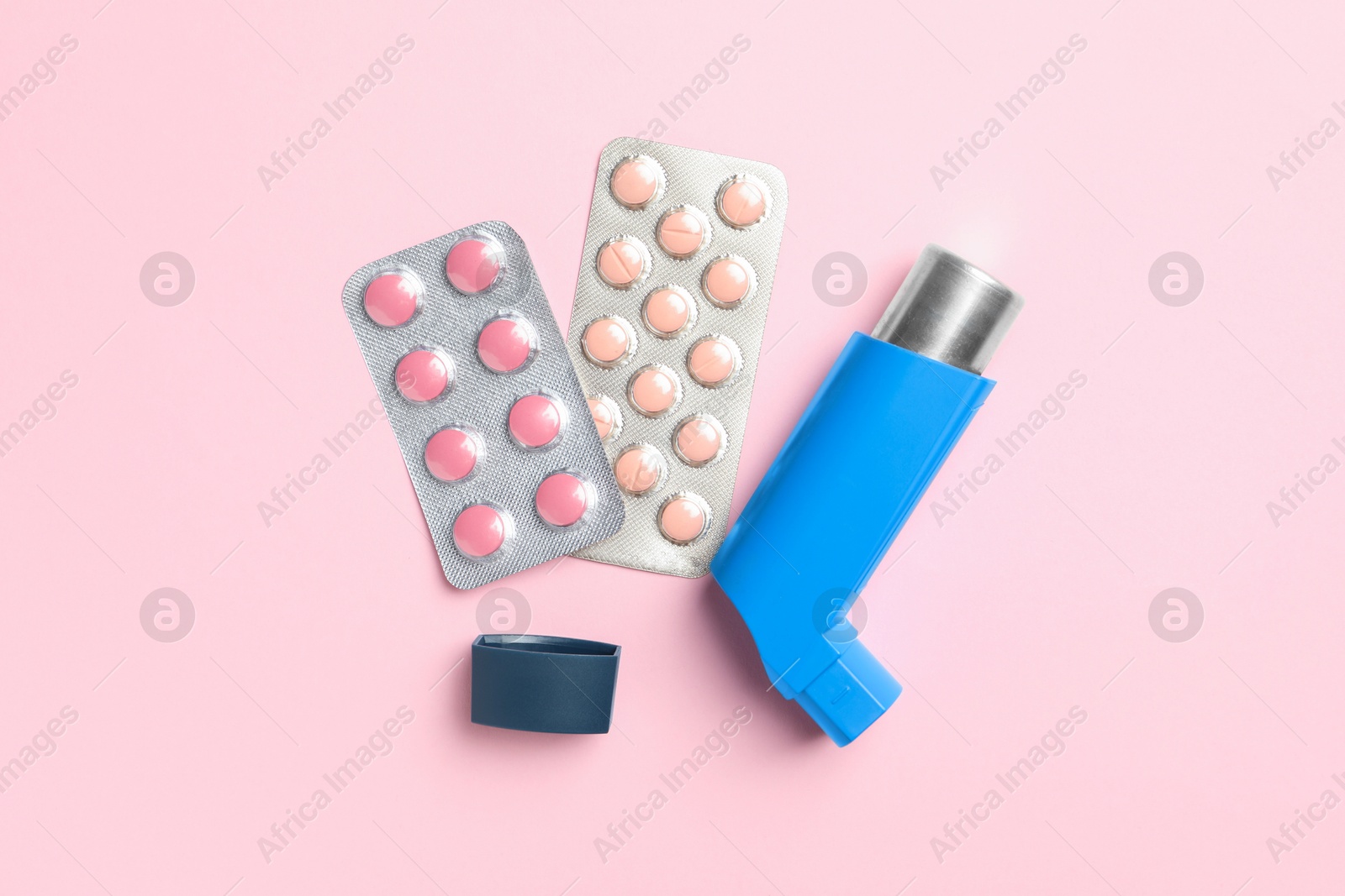 Photo of Asthma inhaler and pills on pink background, flat lay