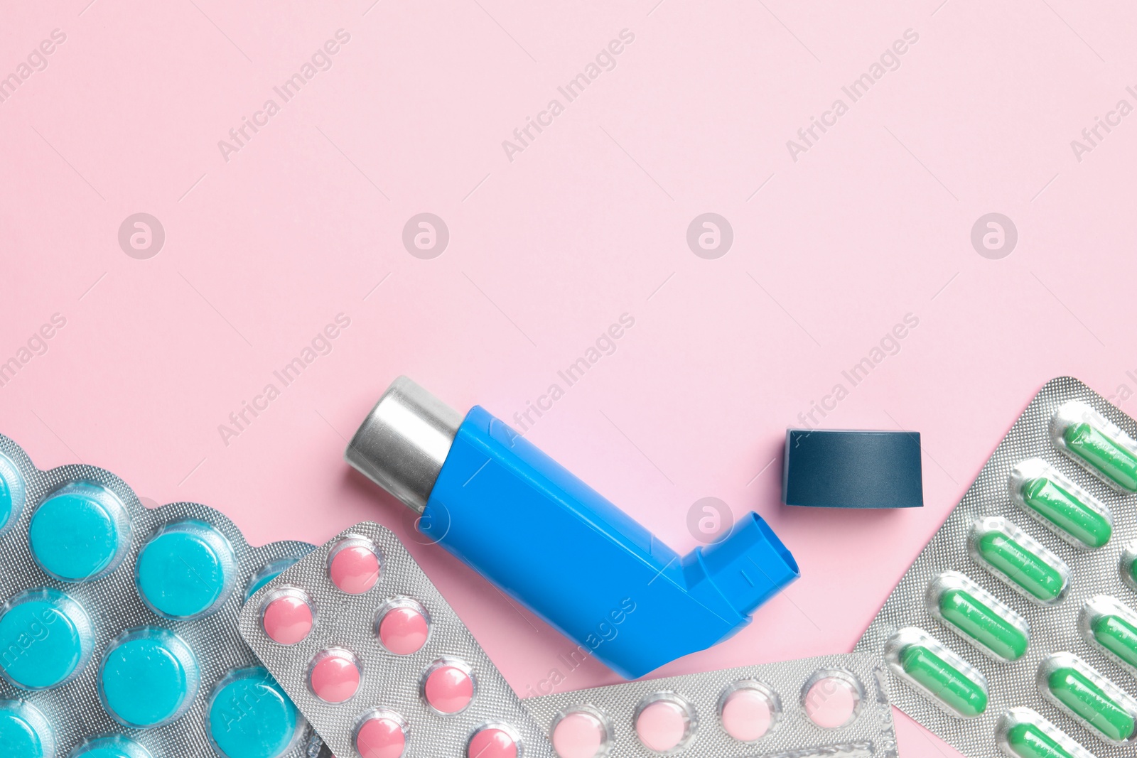 Photo of Asthma inhaler and pills on pink background, flat lay. Space for text