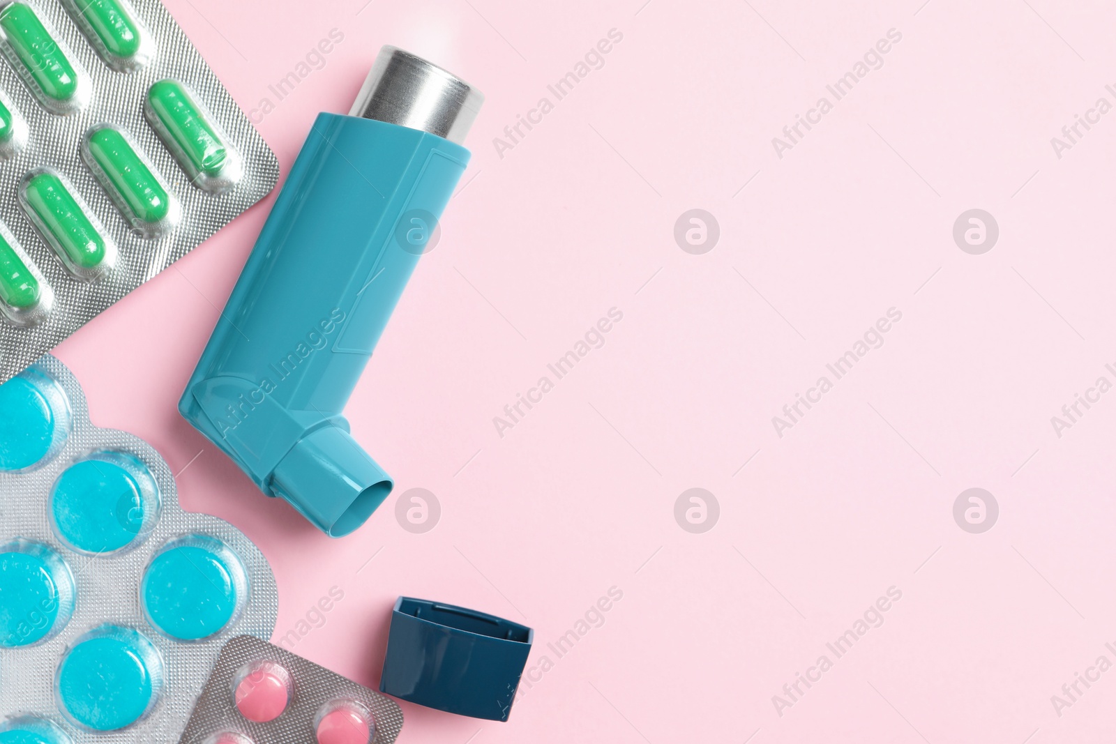 Photo of Asthma inhaler and pills on pink background, flat lay. Space for text