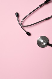 Photo of Stethoscope on pink background, top view. Space for text