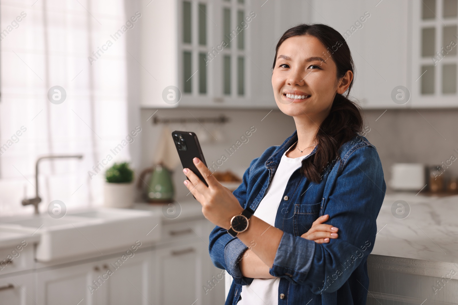 Photo of Smiling woman with smartphone in kitchen. Space for text