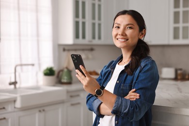 Photo of Smiling woman with smartphone in kitchen. Space for text