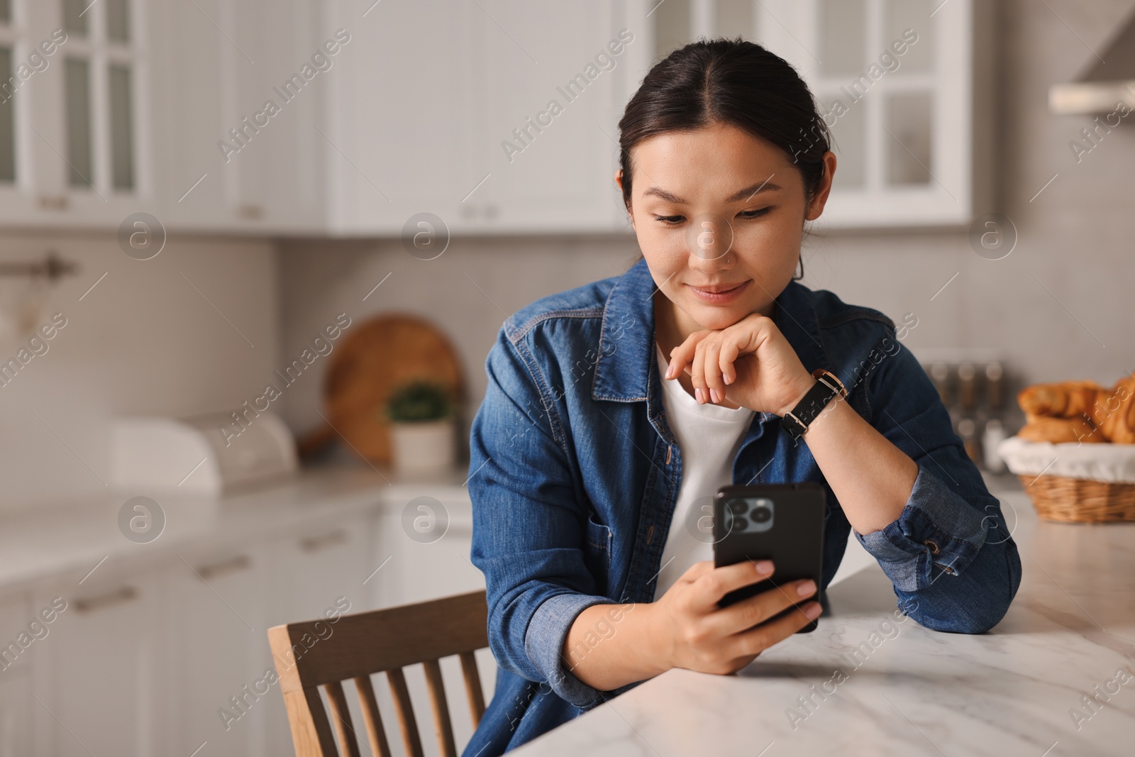 Photo of Beautiful woman using smartphone in kitchen. Space for text