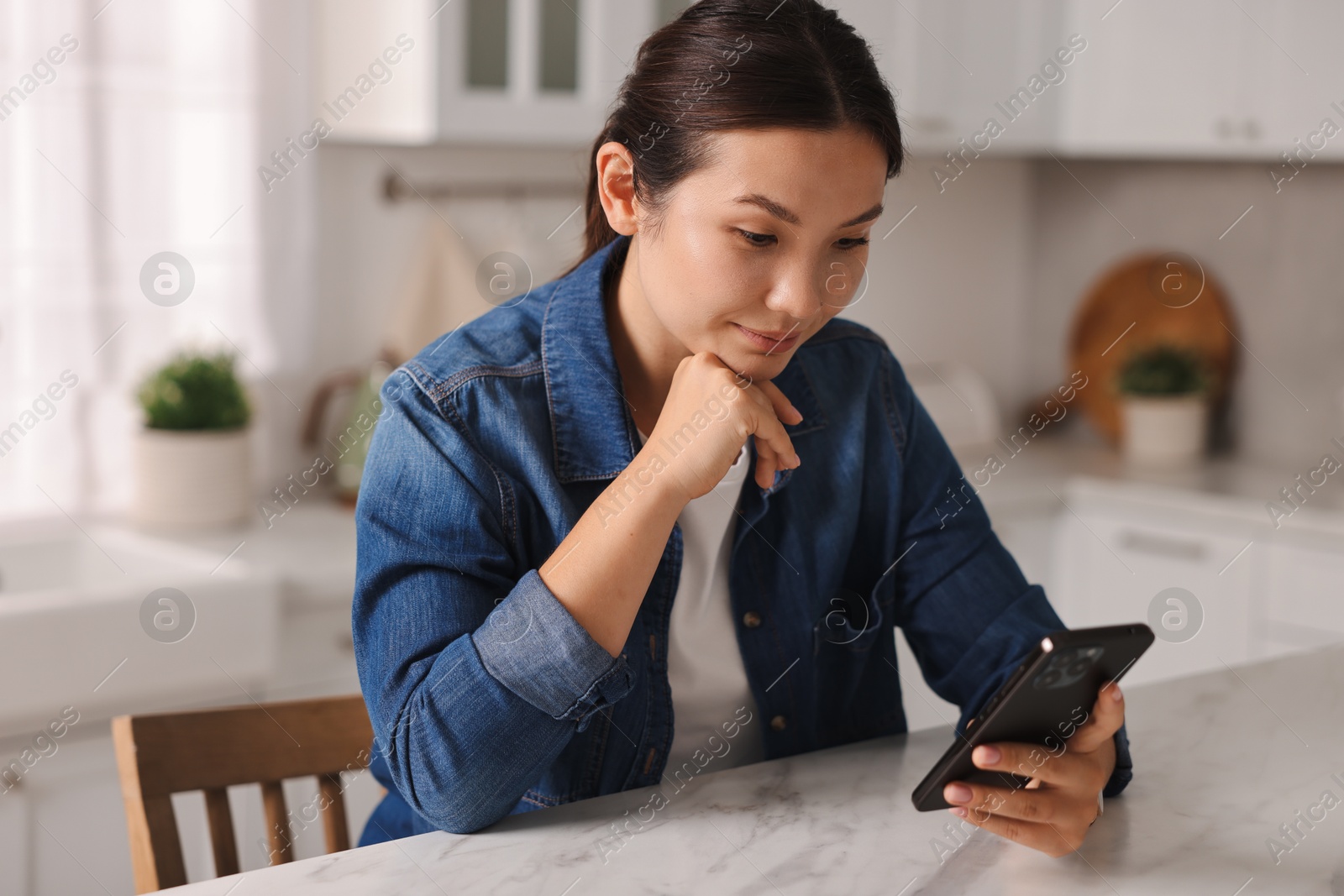 Photo of Beautiful young woman using smartphone in kitchen