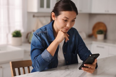 Beautiful young woman using smartphone in kitchen