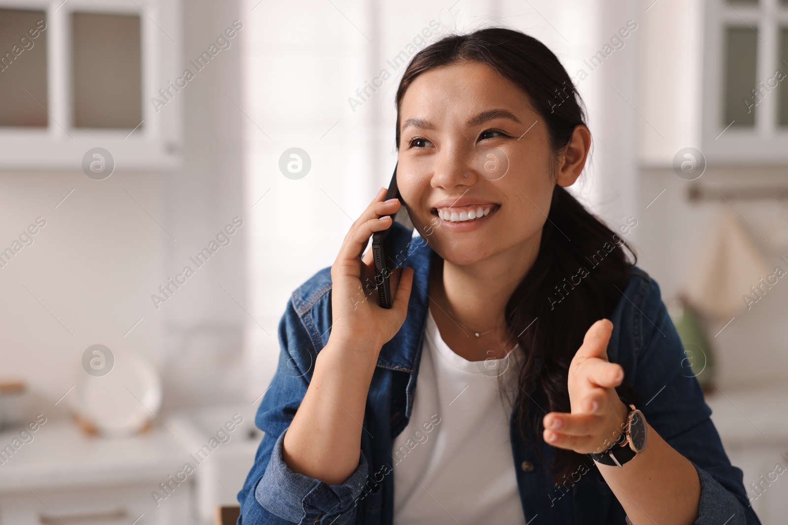 Photo of Smiling woman talking on smartphone in kitchen