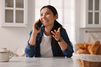 Photo of Smiling woman talking on smartphone in kitchen