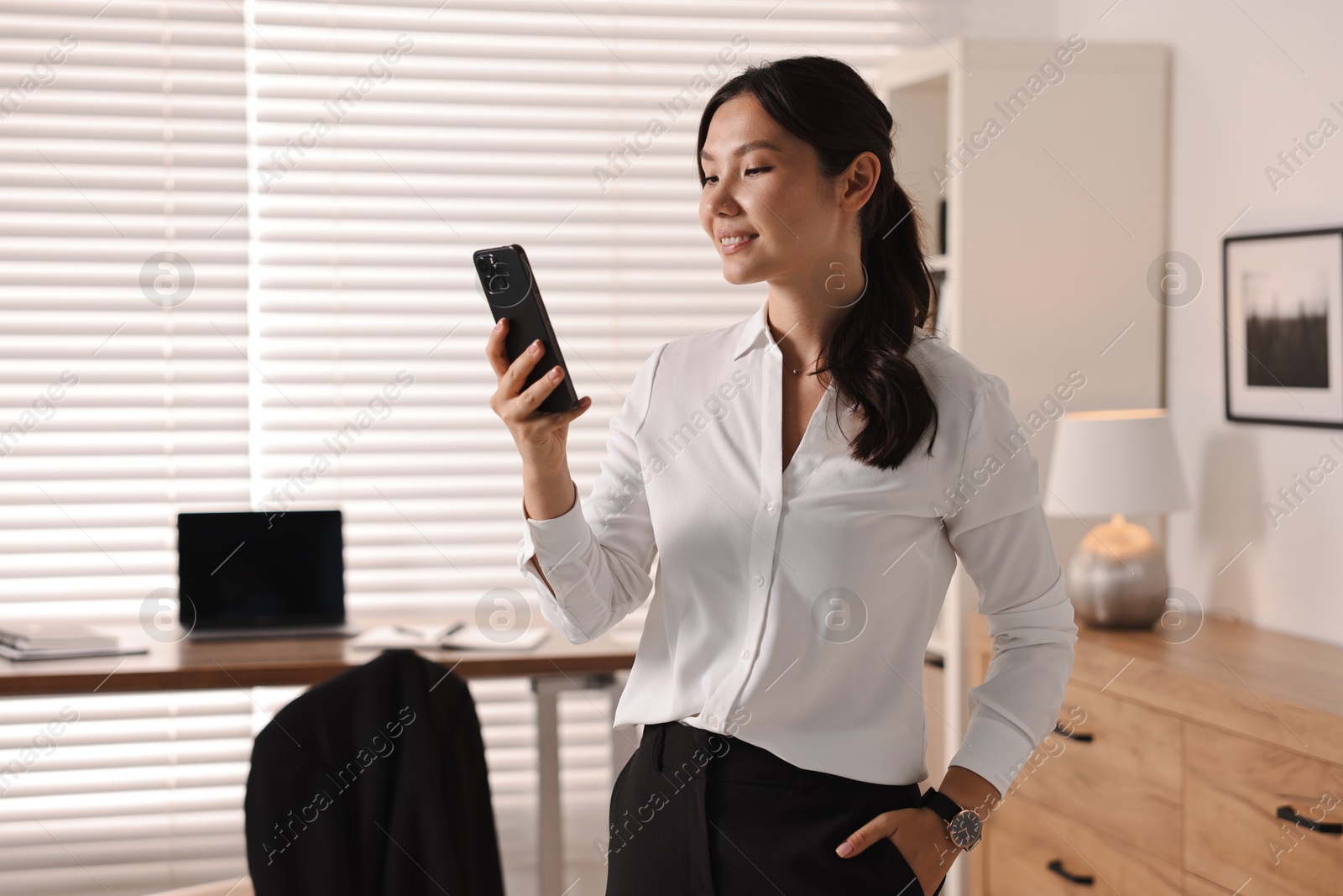 Photo of Smiling young businesswoman using smartphone in office