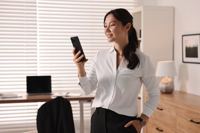 Smiling young businesswoman using smartphone in office