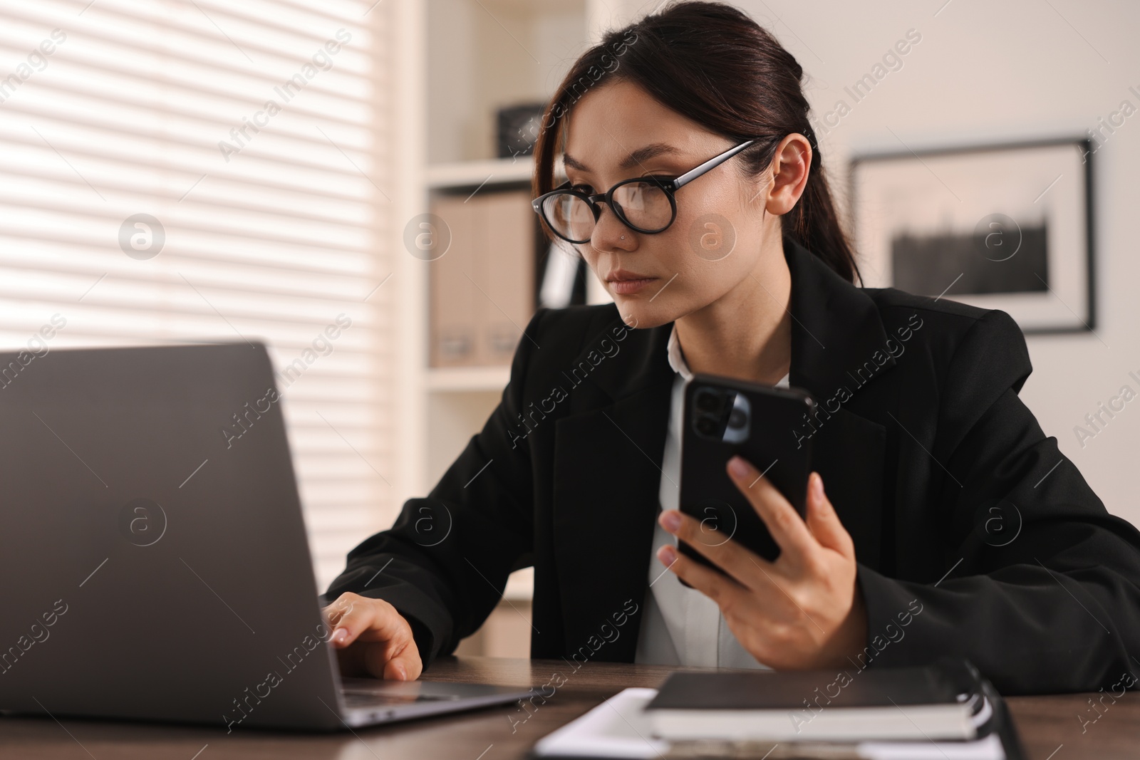 Photo of Beautiful businesswoman with smartphone at table in office