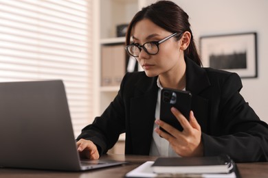 Beautiful businesswoman with smartphone at table in office