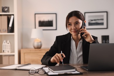 Photo of Beautiful businesswoman talking on smartphone at table in office