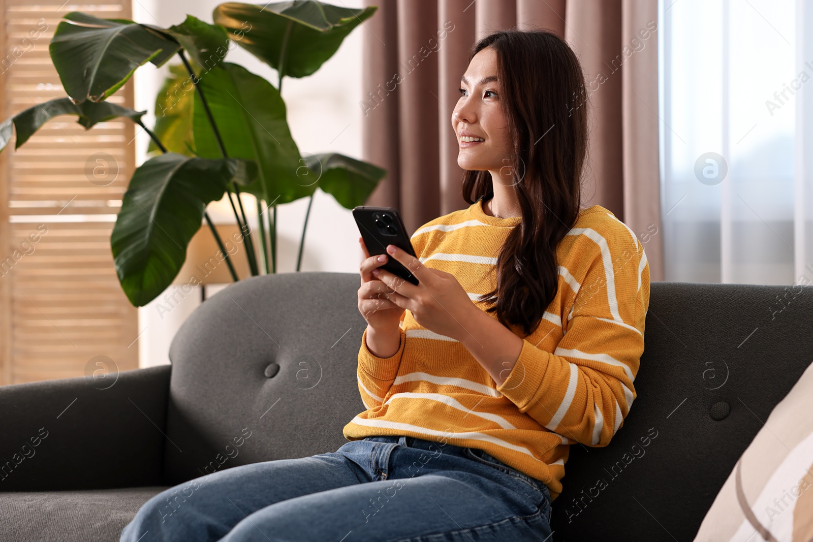 Photo of Smiling woman with smartphone on sofa at home