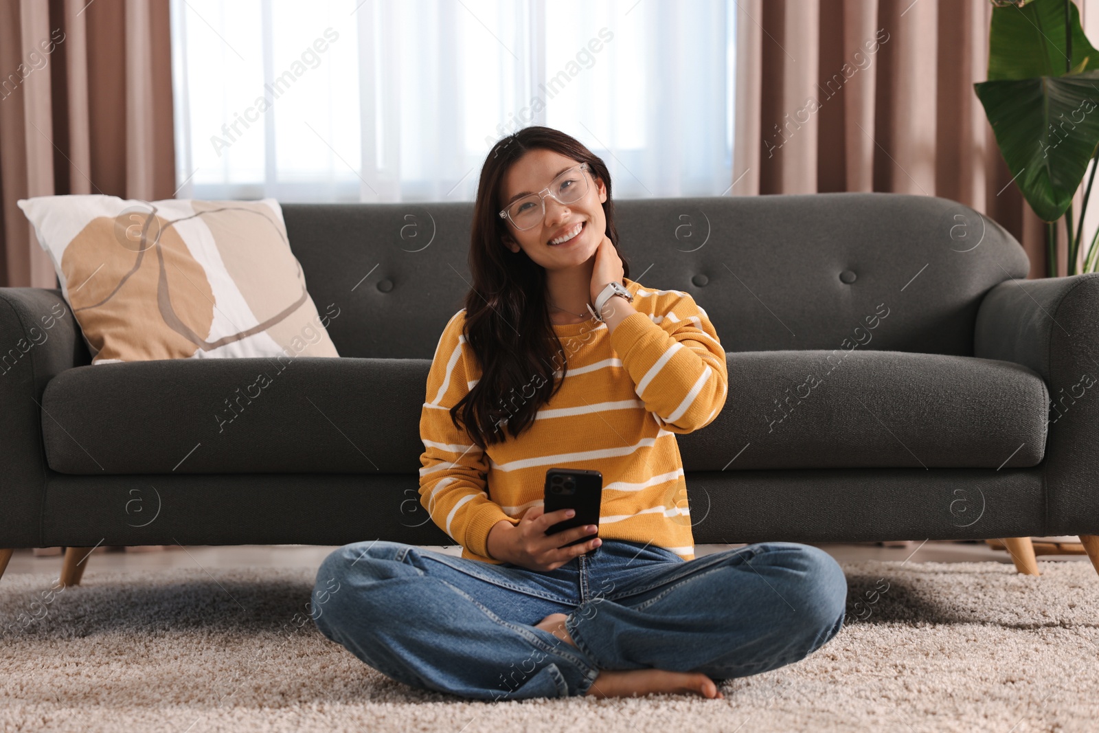 Photo of Smiling woman with smartphone sitting on carpet at home