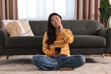 Smiling woman with smartphone sitting on carpet at home