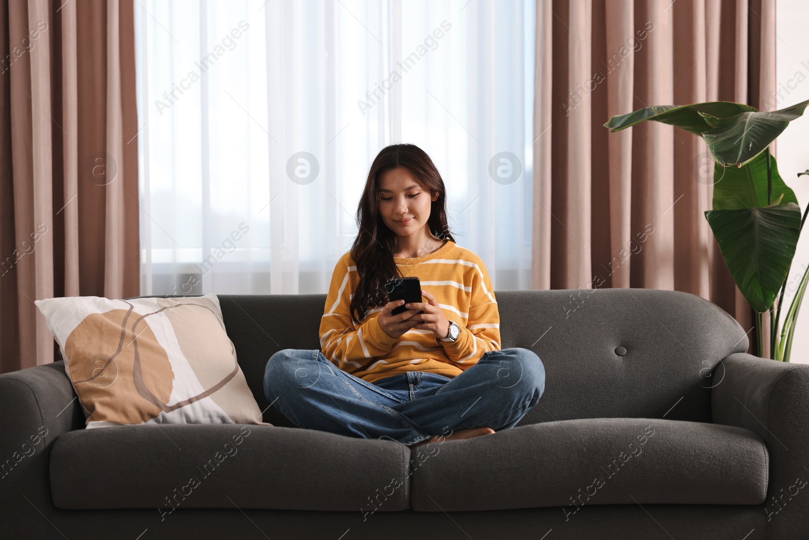 Photo of Beautiful woman using smartphone on sofa at home