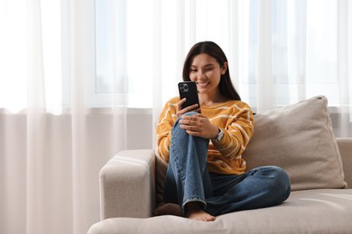 Smiling woman with smartphone on sofa at home. Space for text