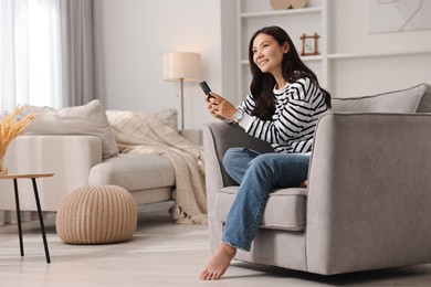 Smiling woman with smartphone sitting on armchair at home