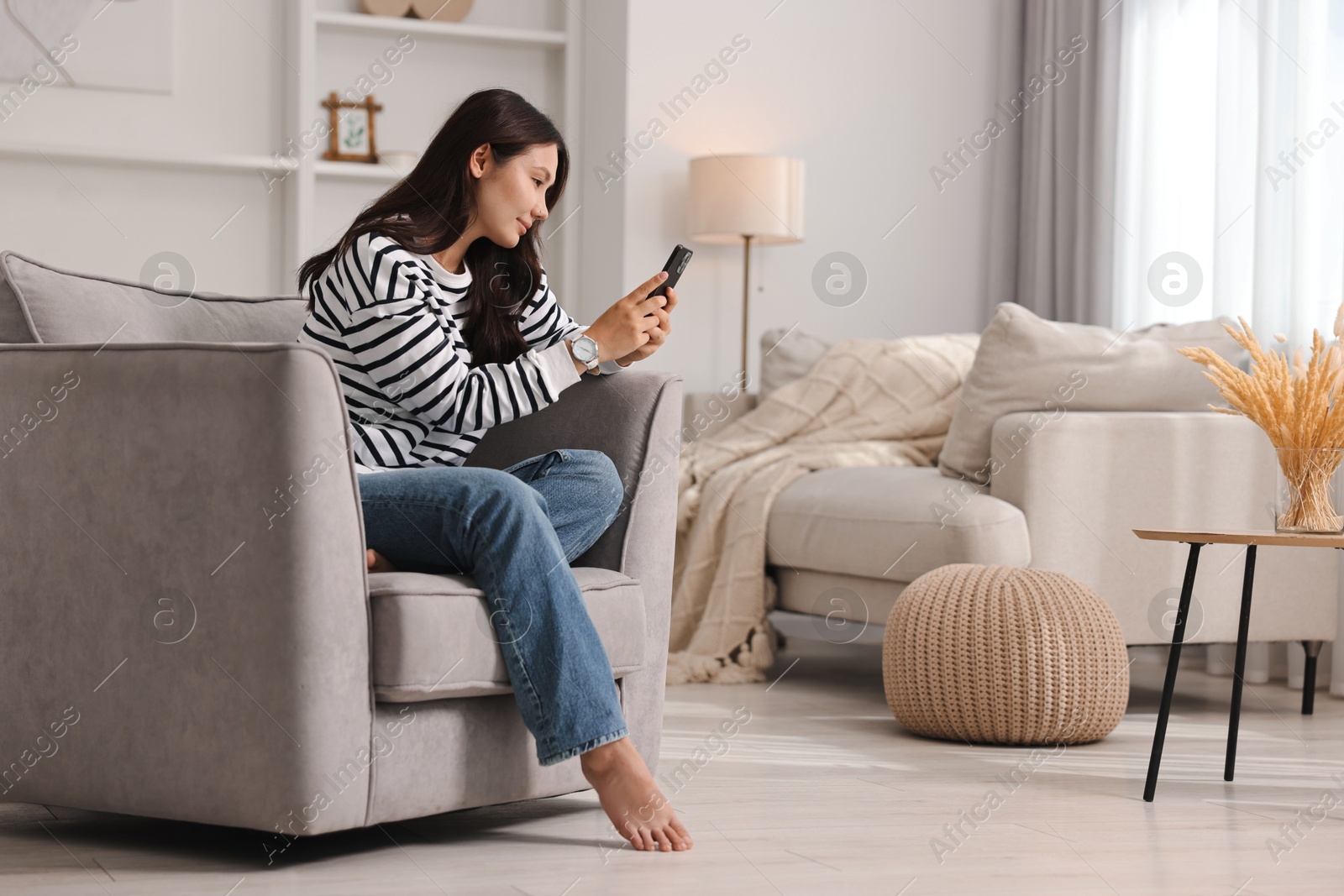 Photo of Beautiful woman with smartphone sitting on armchair at home