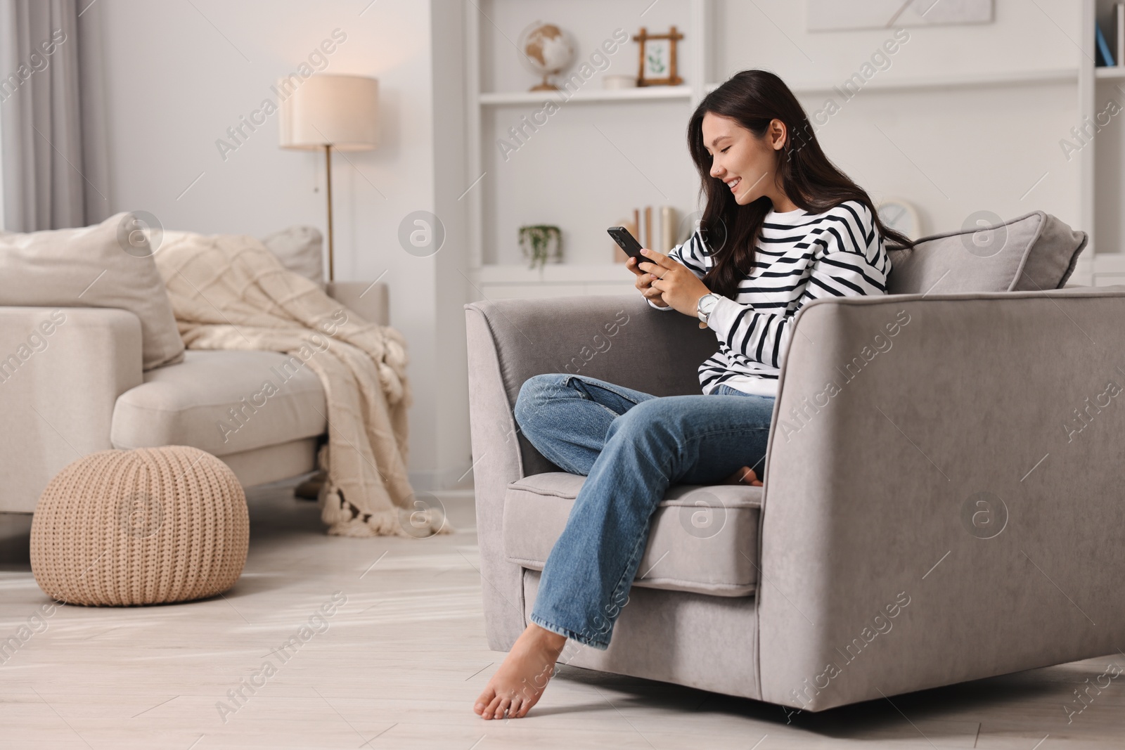 Photo of Smiling woman with smartphone sitting on armchair at home