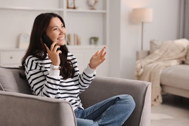 Smiling woman talking on smartphone in armchair at home