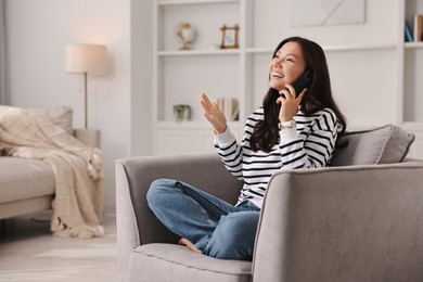 Smiling woman talking on smartphone in armchair at home