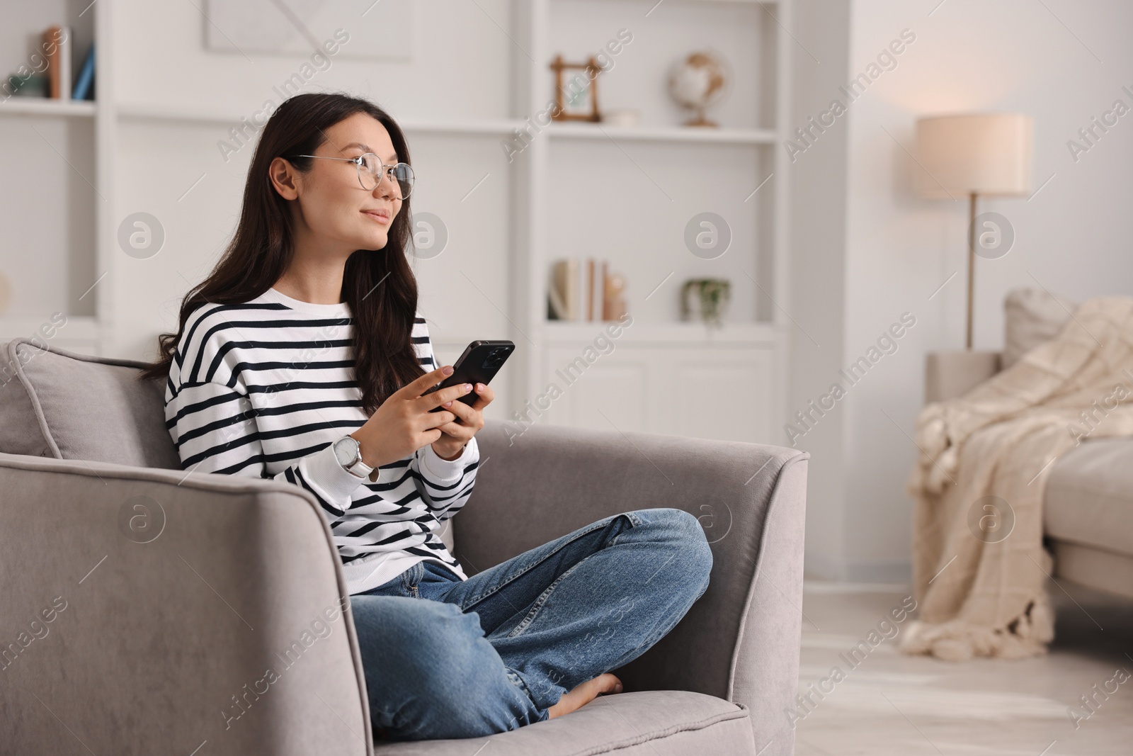 Photo of Beautiful woman with smartphone on armchair at home