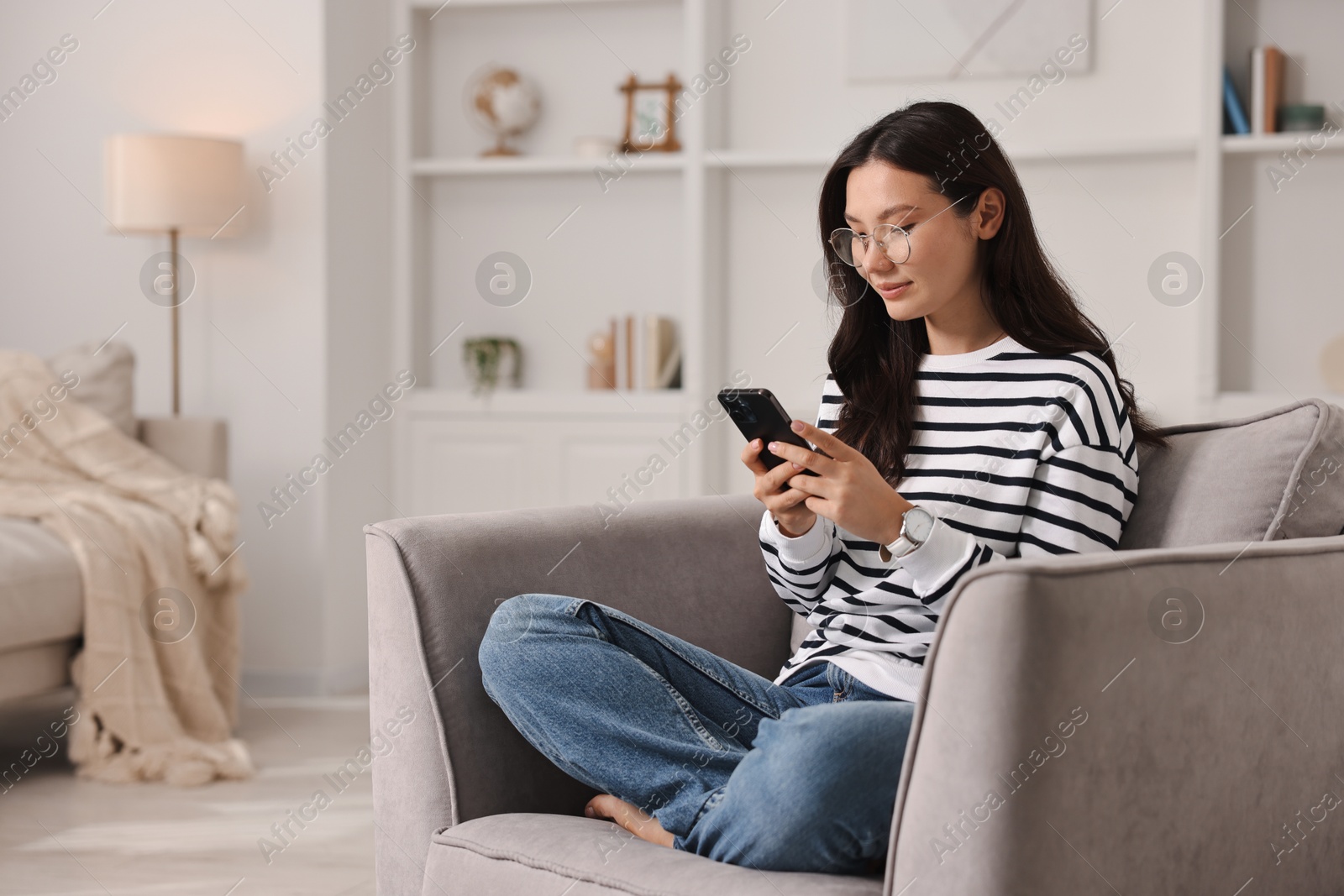 Photo of Beautiful woman with smartphone on armchair at home